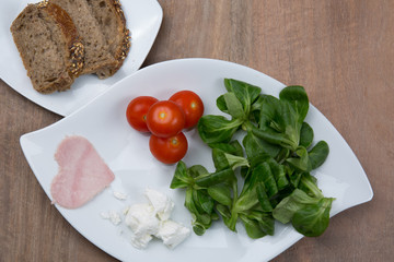 Tomato salad and heart shaped ham on wooden table