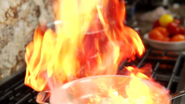 A chef adds some wine to a pan with chicken and flames flare up