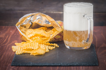 Beer with foam in glass mug and potato chips