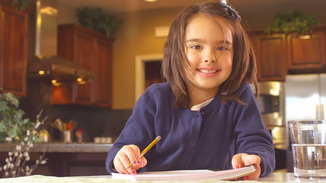 A little girl smiles and then goes back to work on her school workbook