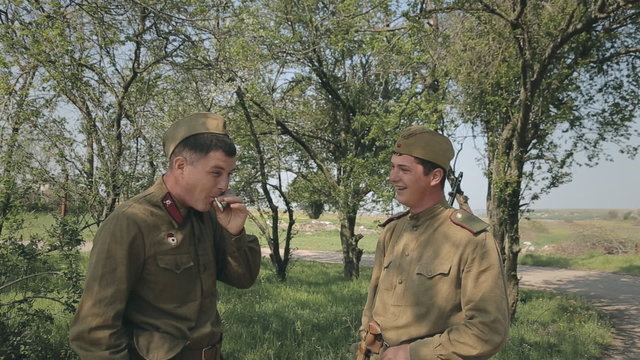 Conversation of two of young soldiers in a forest while smoking