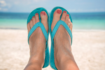 Woman bare sandy feet with blue flip flops, beach and sea 