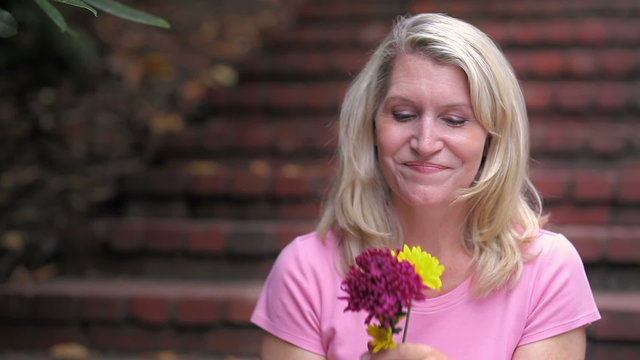 Woman takes a minute to enjoy some sweet smelling flowers. Medium Shot