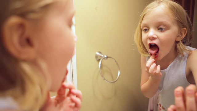 An adorable little girl looks at her teeth in the mirror.