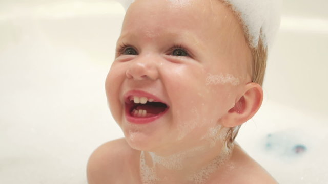 A baby plays with a toy and laughs while taking a bubble bath