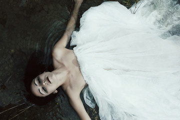 Woman lying on the shore in white dress, dark mystery scene