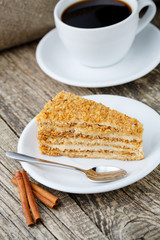 Tasty honey cake with cup of coffee on wooden background.