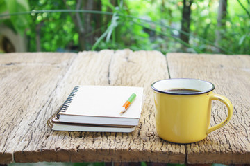 Notebook  and coffee in yellow cup on wooden table