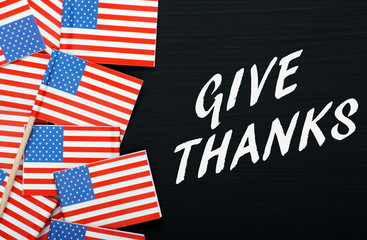 Fototapeta premium The phrase Give Thanks on a blackboard with USA flags