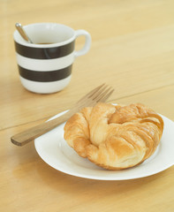 Croissant on white plate and cupof coffee.