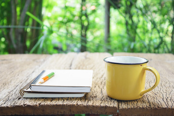 Notebook  and coffee in yellow cup on wooden table
