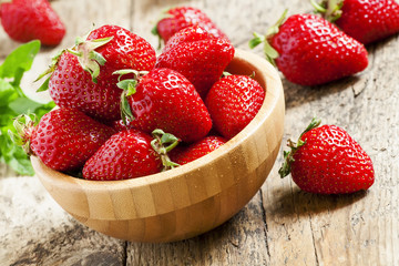 Fresh strawberries in a wooden bowl on a wooden table in rustic