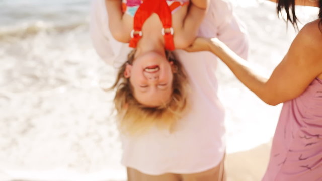 Little girl on her dad's shoulders gets tickled by her mom. 