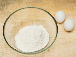 Bowl of flour and white eggs on a wood kitchen table