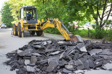 yellow excavator removes the debris the asphalt road in city