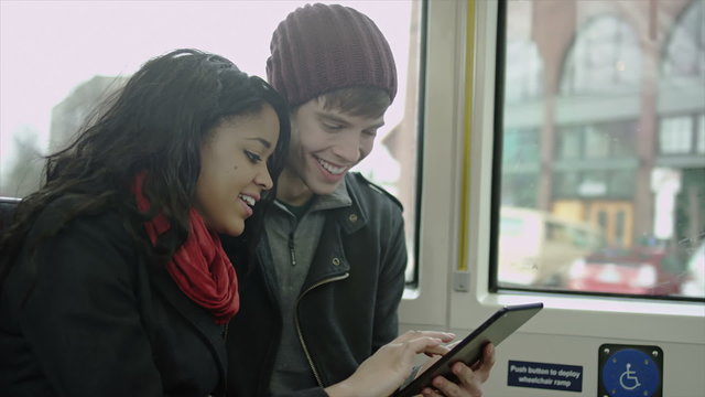A couple has fun playing with their tablet computer as they ride the bus