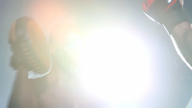 Two sweaty boxers spar in the ring with a giant bright light behind them