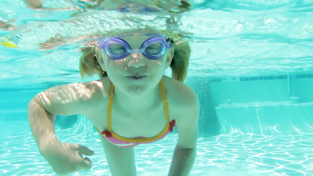 A young girl swims towards the camera while underwater