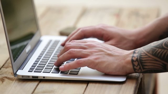 close up image of hands of a tattooed man using laptop