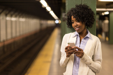 Young African American black woman in city at night texting cell phone subway station