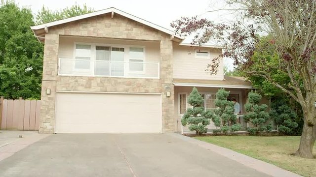 A family of four come out from their house and walk down their driveway to smile and wave into the camera