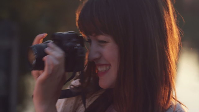 Close up of a young woman taking pictures with her camera at sunset