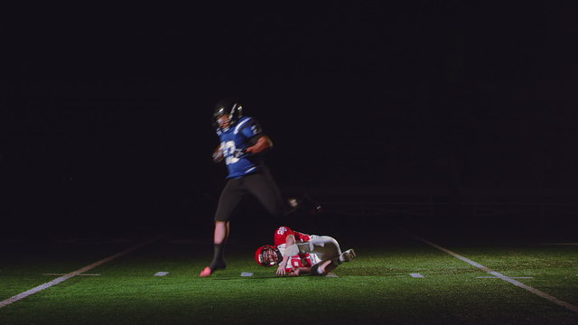 Football player effortlessly leaps over a tackle attempt in slow motion running a play in the dark