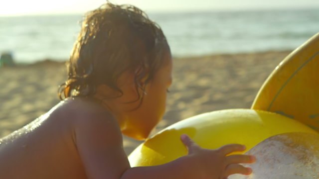 A young boy plays with a large beachball in the sand