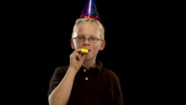 A young blonde boy wears a party hat and blows a noisemaker party favor