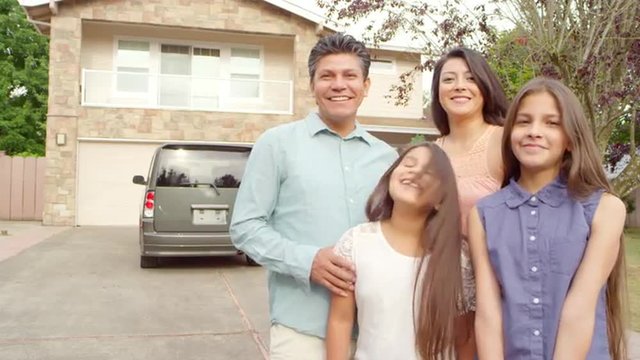 A family stands outside in their driveway looking and smiling at the camera