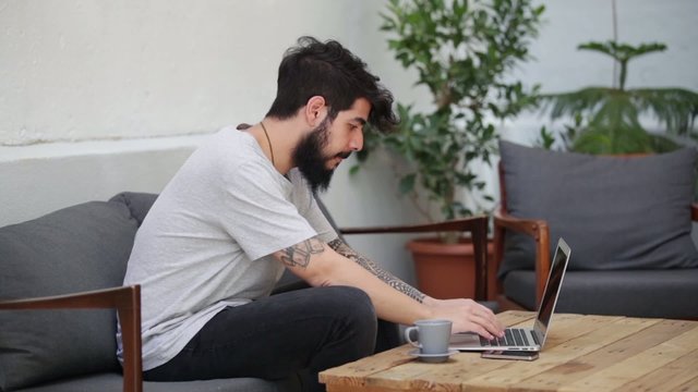 young tattooed guy using a laptop and a smartphone