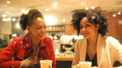 Two girls laugh hysterically together in a coffee shop