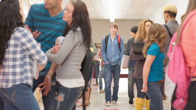 Friends walk through a crowd of students standing in the hallway before class