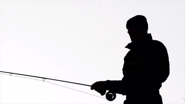 Slow motion shot of a man fly fishing in a river, silhouetted against the sky