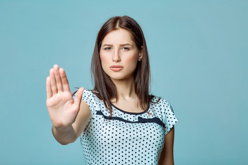 Young woman making stop gesture with her palm, on a blue 