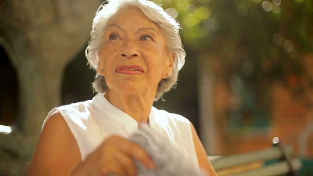 An old lady sits on a bench and fans herself in the heat