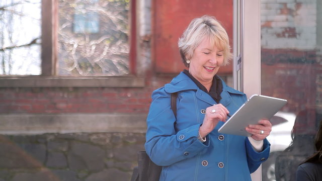 An Older Woman Uses Her Tablet While Waiting For The Bus