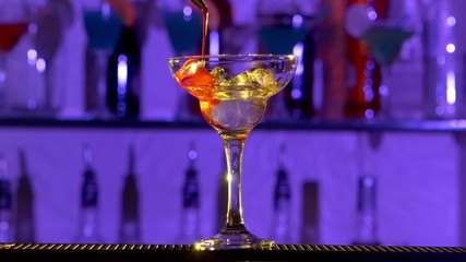 Barman making cocktail in a glass using ice, sweet syrup and