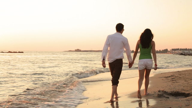 A young couple walking on the beach barefoot during magic hour