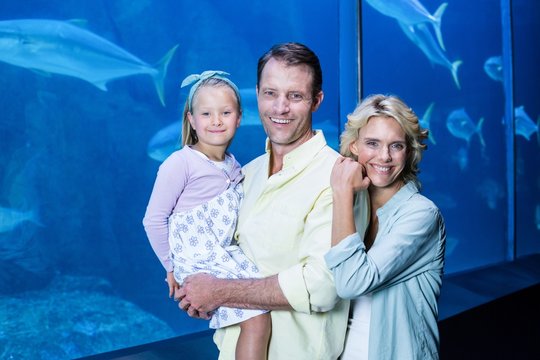 Happy family looking at camera beside the fish tank