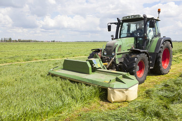 Naklejka premium tractor and mower in green meadow in holland