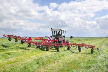red hay turner in green grass field in the netherlands