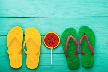 Colorful flip flops and candy on blue wooden floor. Top view and summer accessories