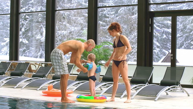 A father and mother getting their son ready to swim in a pool with snow outside