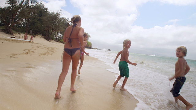 Four Young Kids Run Down The Beach Away From The Camera