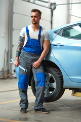 Portrait of a mechanic standing against a car at his workshop