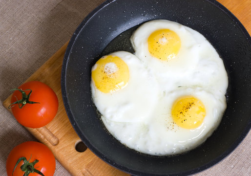 Three fried chicken eggs in a pan on a wooden board  