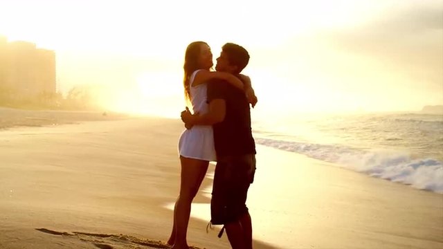 Brazilian couple embrace on a beach in Brazil bathed in warm yellow sunlight