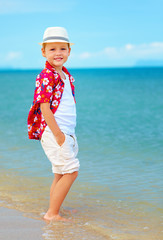 Fototapeta na wymiar cute fashionable boy stands in surf on summer beach
