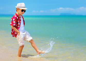 happy fashionable kid boy walking in surf on tropical beach © Olesia Bilkei